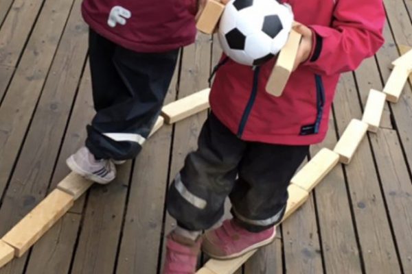 Förskolebarn leker utomhus med fotboll