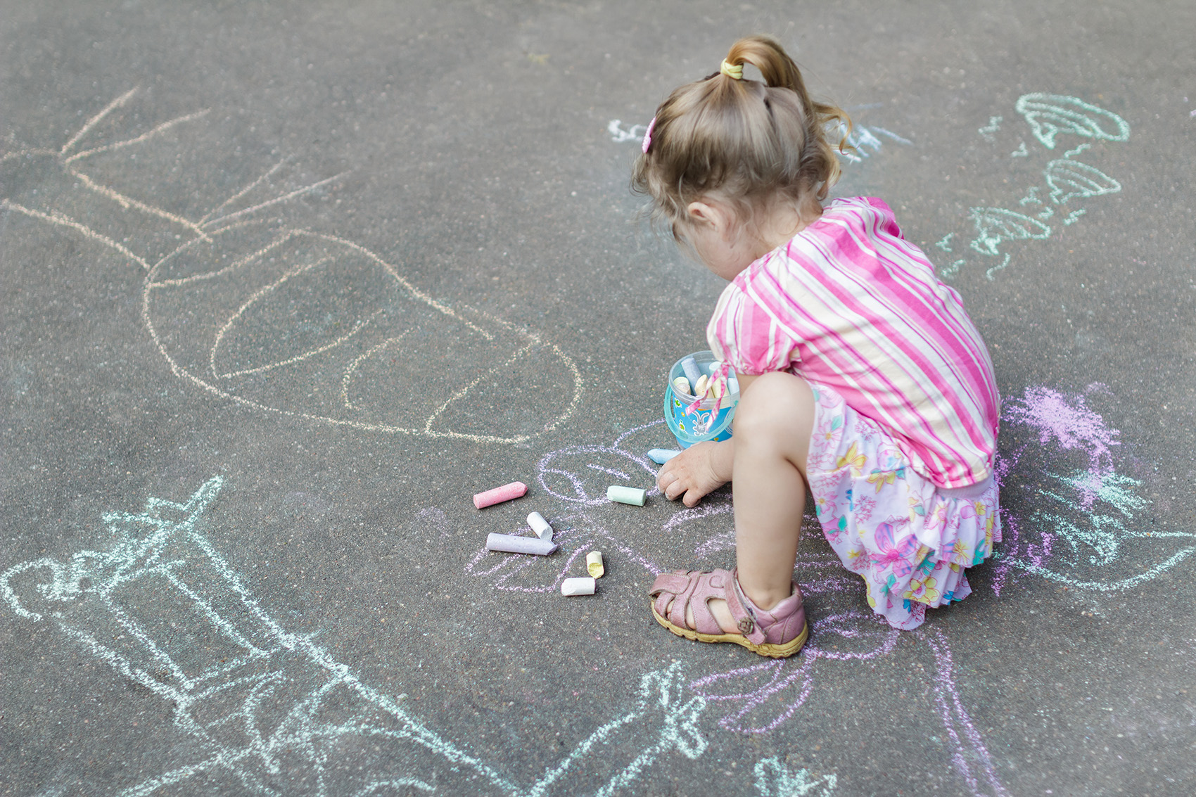 Flicka i förskoleålder ritar med färgglada kritor på asfalten på förskolans skolgård